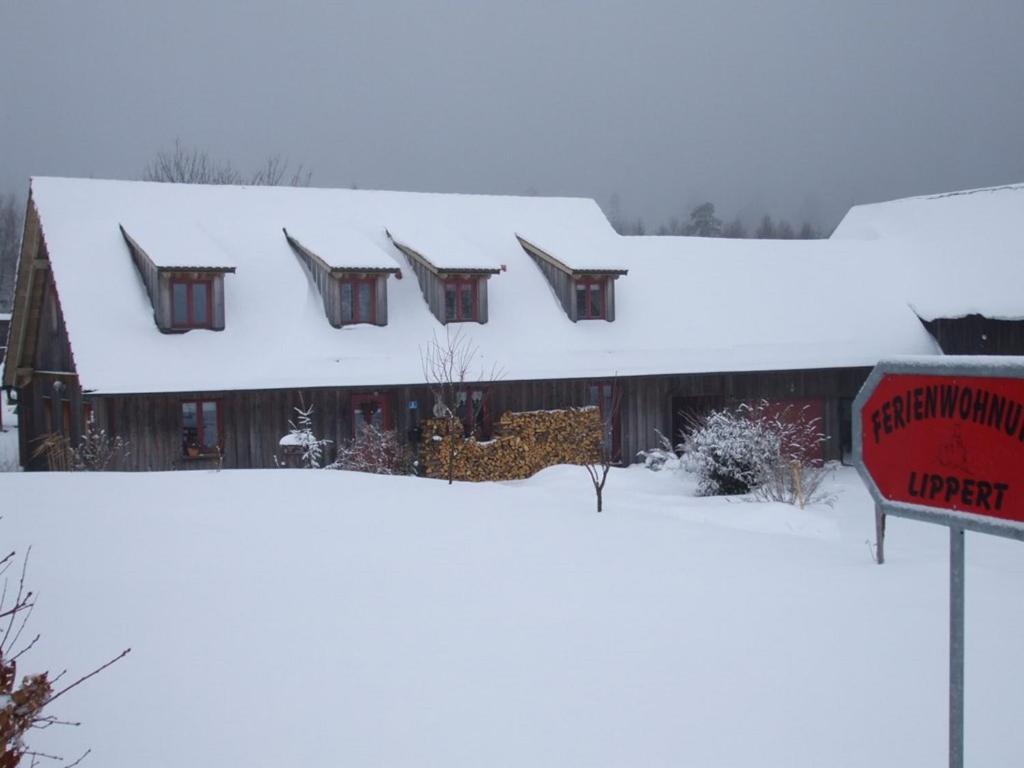 a house covered in snow with a sign in front at Ferienwohnung Lippert in Pullenreuth