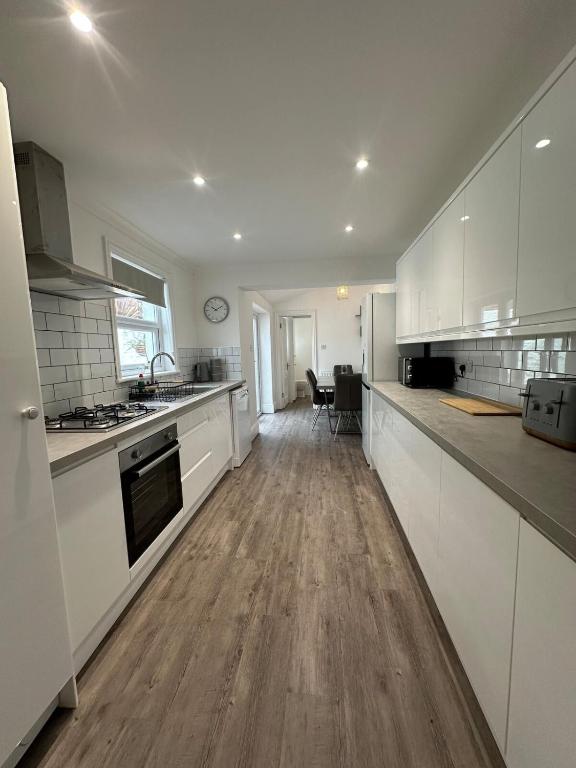 a kitchen with white cabinets and a wooden floor at 3 bed Spacious House with Parking in Worthing