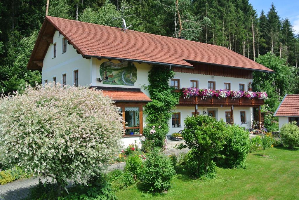 a white house with a red roof and flowers at Haus Am Waldrand - Ferienwohnung Augustin in Grafenau