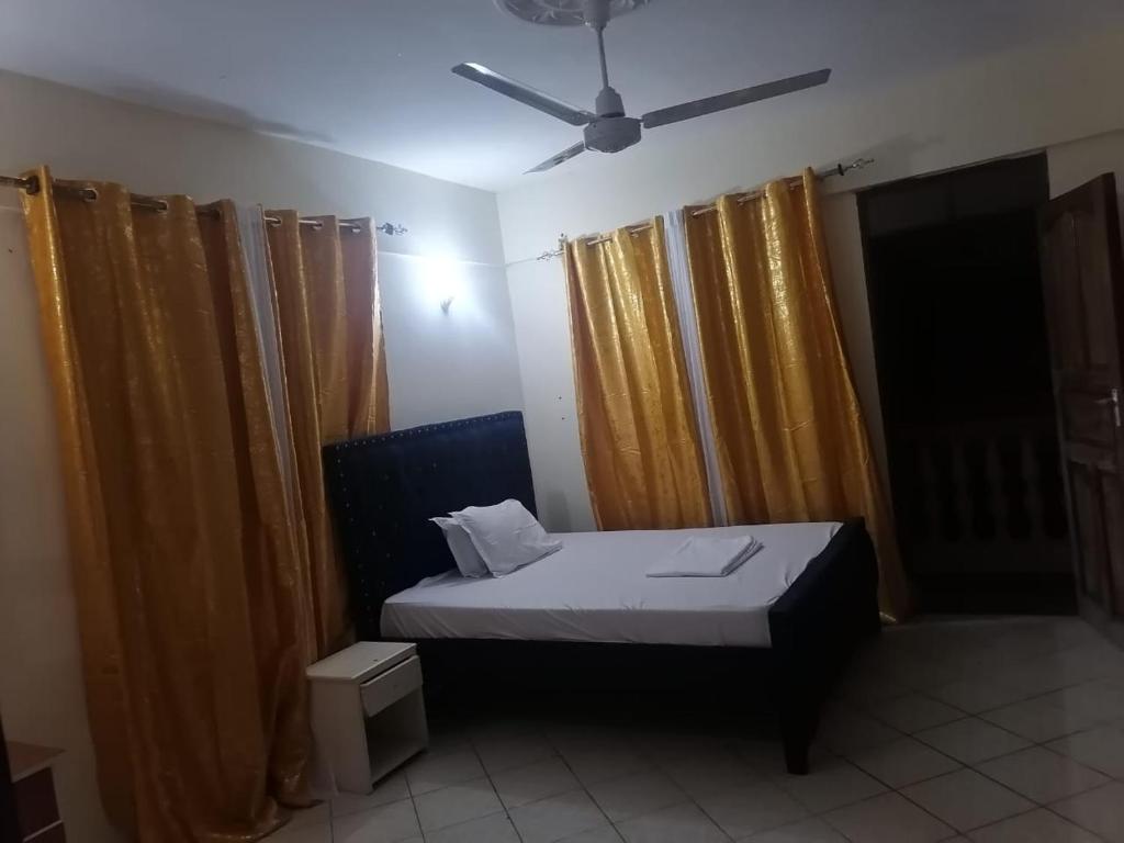 a bedroom with a bed and curtains and a ceiling fan at La Grande Cosy 1 Bedroom Ensuite Mtwapa in Mtwapa