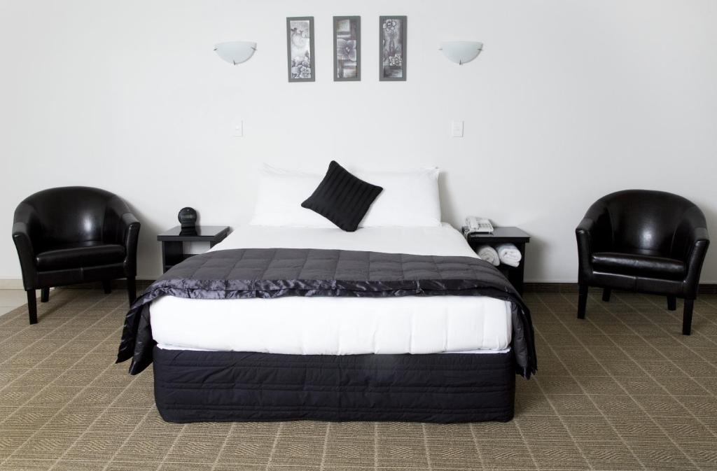 a bedroom with a bed and two black chairs at Hygate Motor Lodge in Hamilton