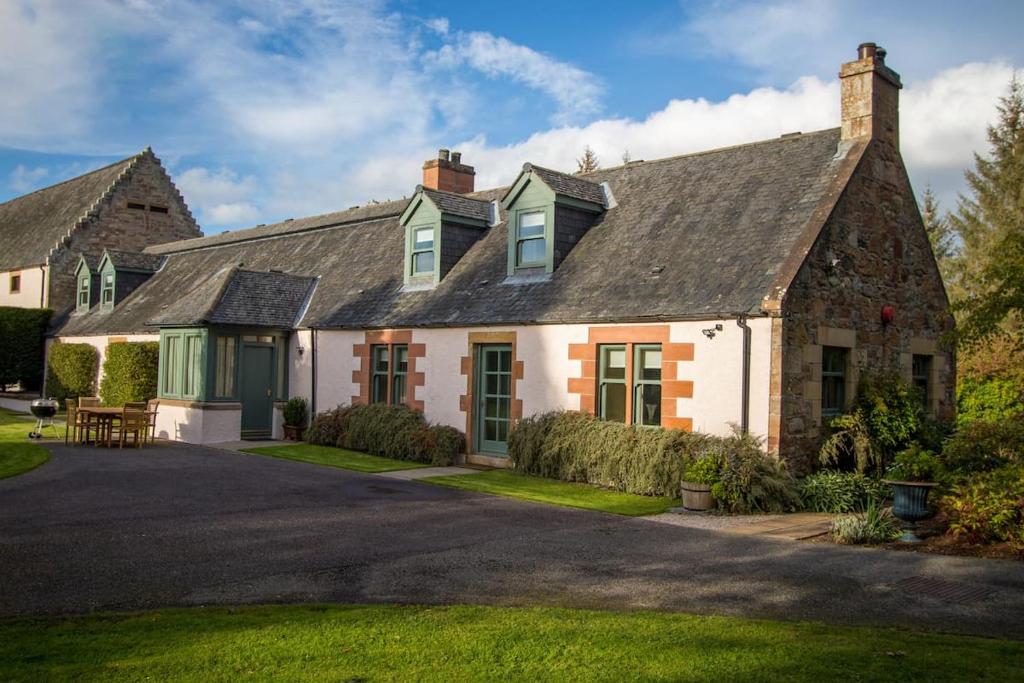 ein altes Steinhaus mit grünen Türen und einem Hof in der Unterkunft Grieves Cottage Balnagown Estate in Kildary