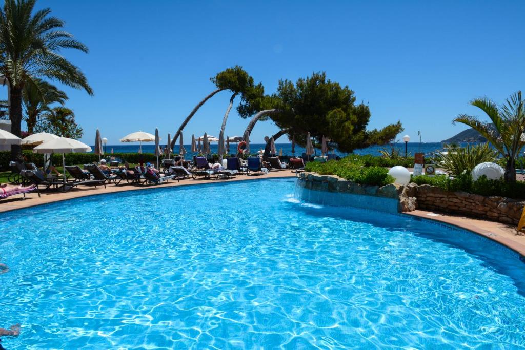 a swimming pool at a resort with palm trees and chairs at Catalonia Ses Estaques - Adults Only in Santa Eularia des Riu