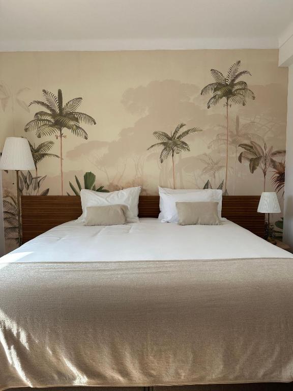 a bedroom with a large white bed with palm trees on the wall at Charm-In Apartments in Vila Nova de Milfontes