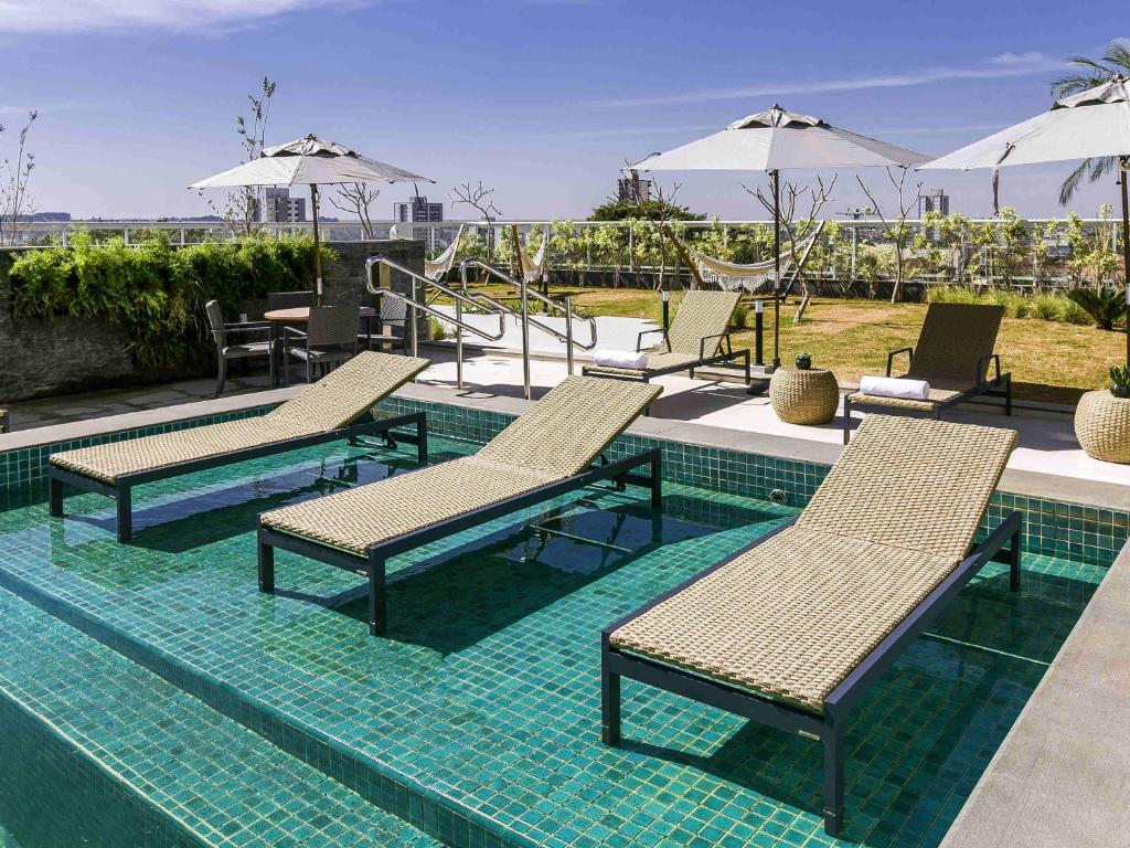 a pool with chairs and tables and umbrellas at Novotel Lencois Paulista in Lençóis Paulista