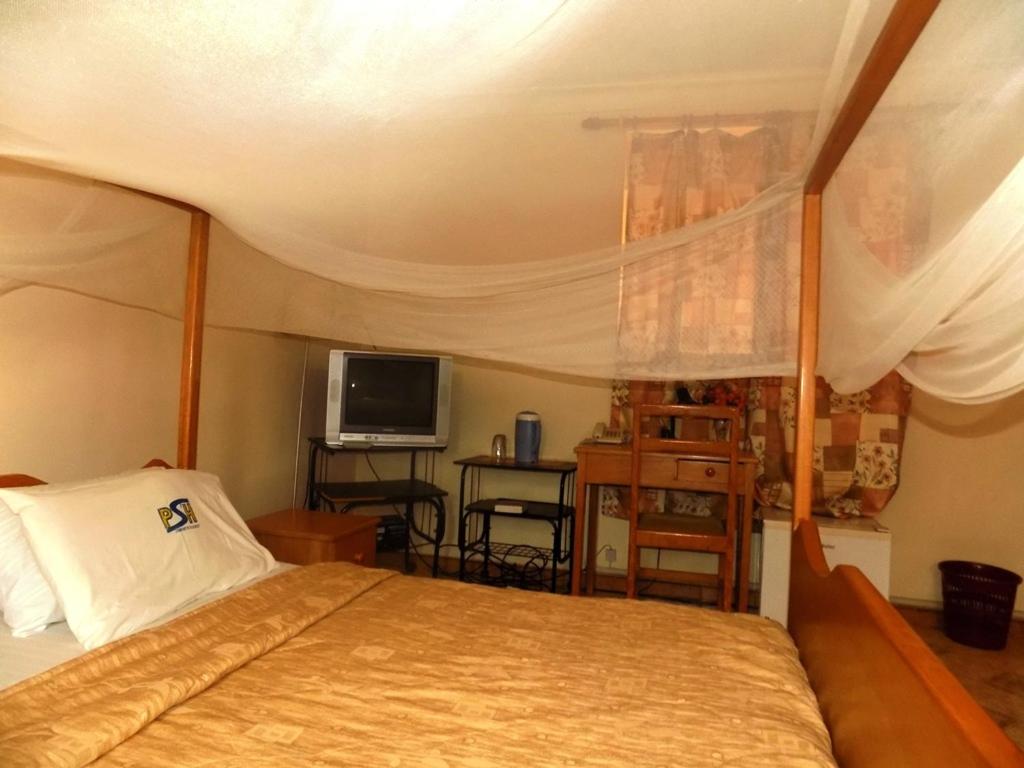 een slaapkamer met een bed en een televisie bij Palm Springs Hotel Masaka in Masaka