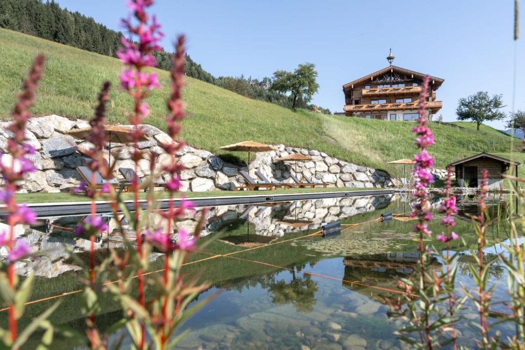 a house on a hill next to a pond with purple flowers at Das Grabnergut - Sommerkarte der Gasteiner Bergbahnen inklusive in Bad Hofgastein
