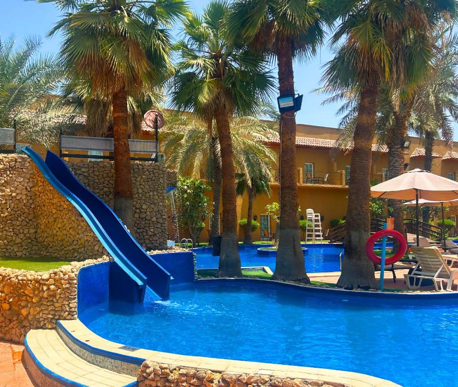 a slide in a swimming pool with palm trees at Montrose - A Mayfair Collection Hotel in Kuwait
