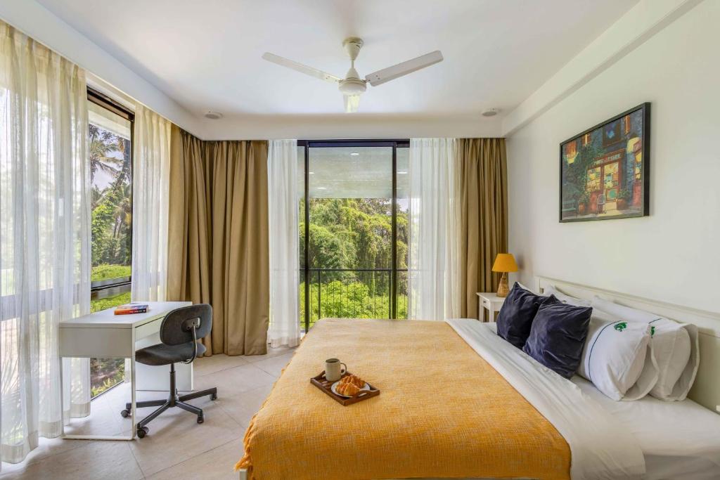 a bedroom with a bed and a desk and a window at Tastefully Done 1BHK Apartment by tisyastays in Candolim