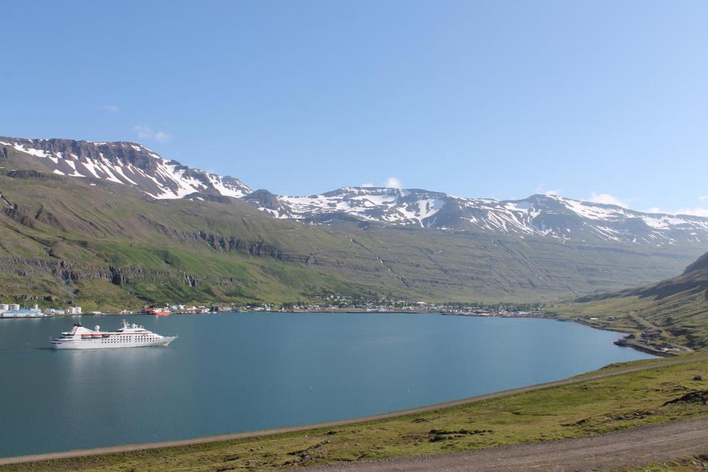 a boat in a lake with mountains in the background at Langahlid Cottages & Hot Tubs in Seyðisfjörður