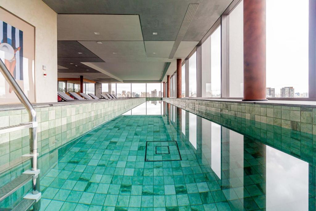 uma piscina com piso de ladrilho verde e janelas em Charlie For You Moema em São Paulo