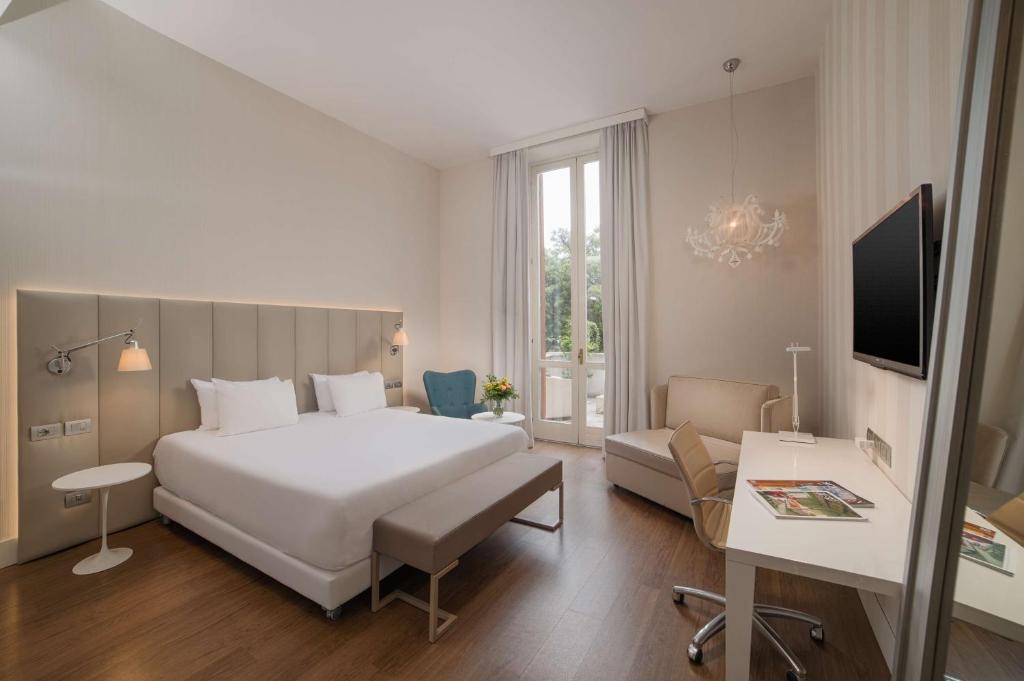 a bedroom with a large white bed and a living room at NH Genova Centro in Genova