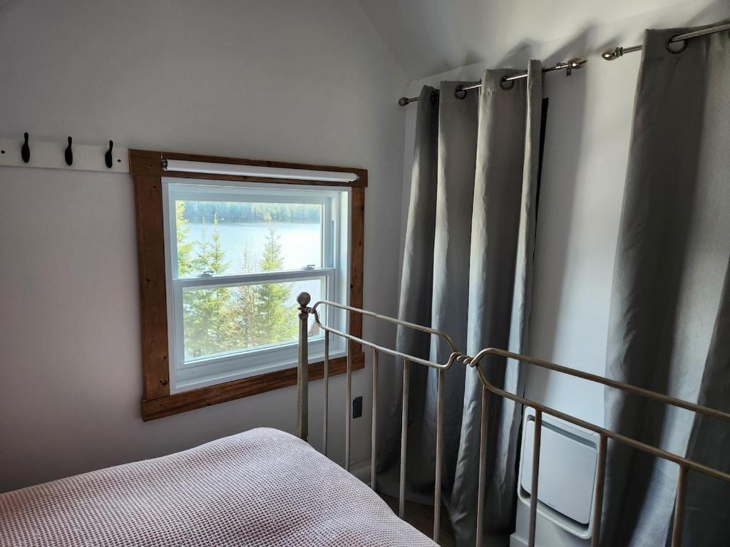 een slaapkamer met een bed en een raam met gordijnen bij Chalet Lac Édouard cozy in La Tuque