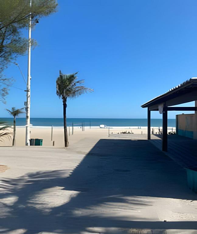 a beach with a pavilion and palm trees and the ocean at Duplex em Itaúna 4min da Praia que ocorre o WSL, 1min da pista de skate do LS, pracinha com parque infantil, quadra de futebol, tudo isso a 1 min da duplex, perto do comércio, wi-fi super rápido, monitoramento 24hrs in Saquarema