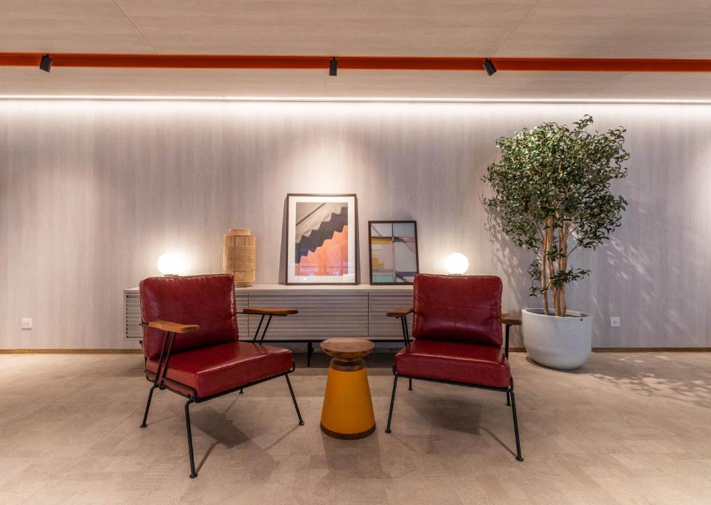 Two red lounge chairs form a small conversational seating area beside a console and indoor tree.