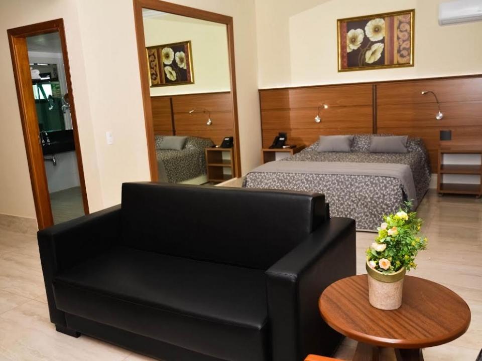 a bedroom with a bed and a couch and a table at Tamareiras Prime Hotel in Uberaba