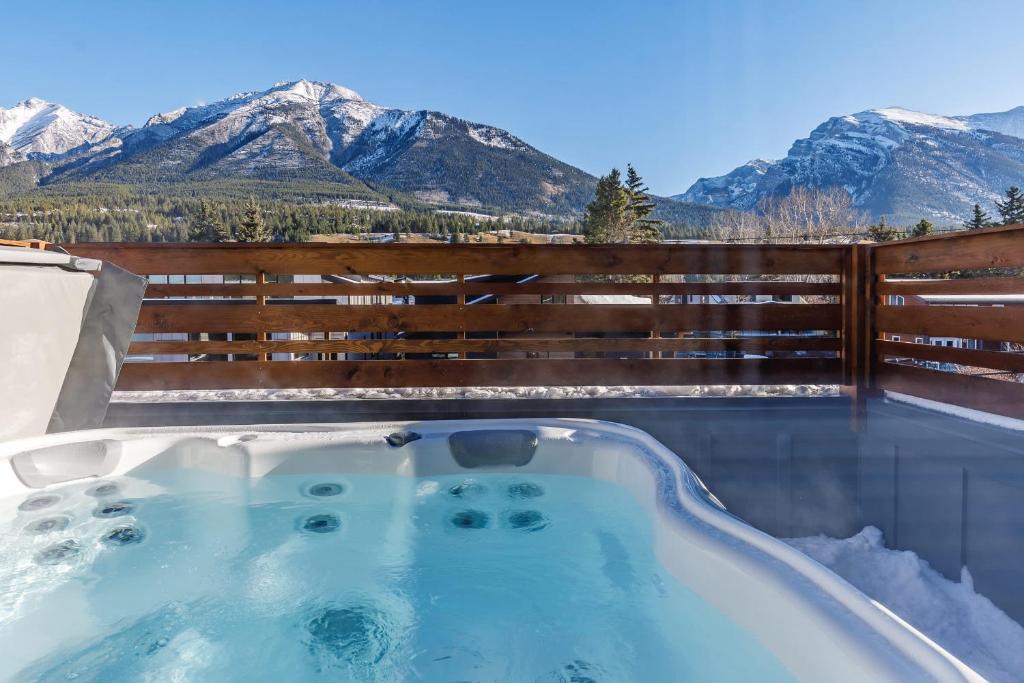 a hot tub with snow covered mountains in the background at Aurora Luxe - Stunning Townhouse Private Hot Tub in Canmore