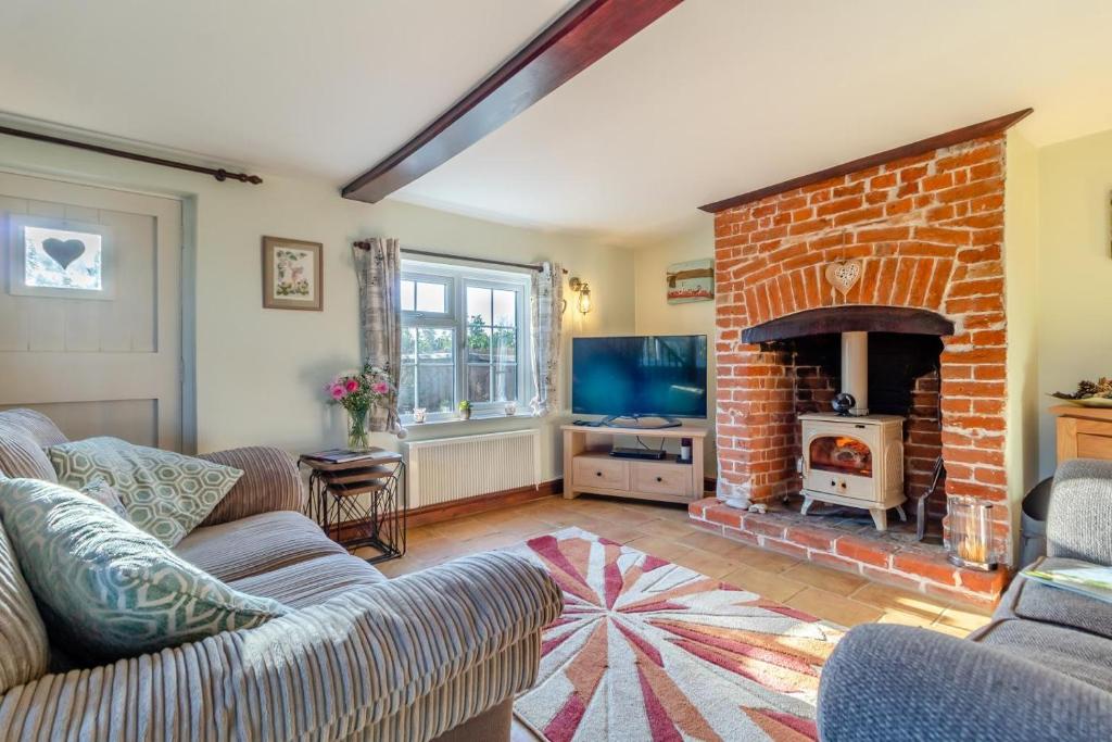 a living room with a couch and a brick fireplace at Valentine Cottage in Snape
