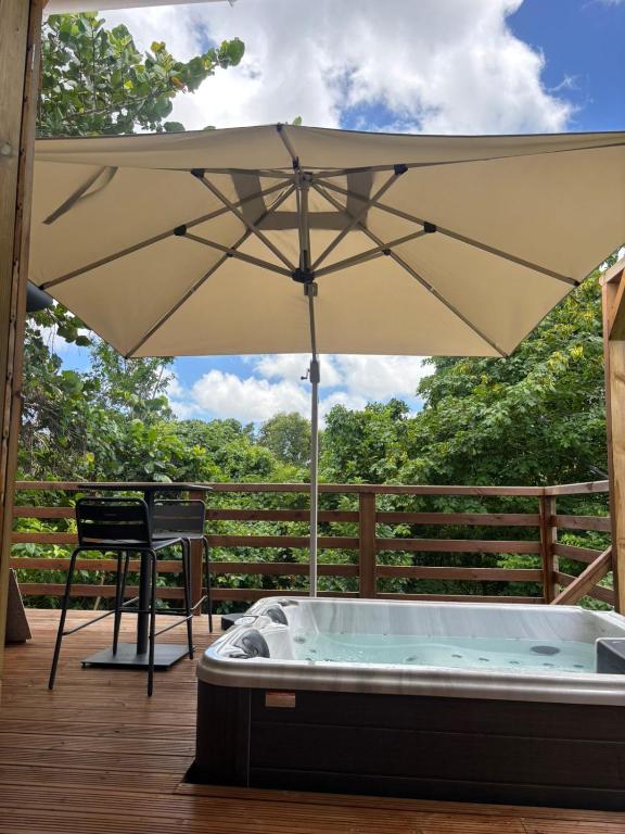 a hot tub with an umbrella on a deck at La pause verte bungalow in Sainte-Anne