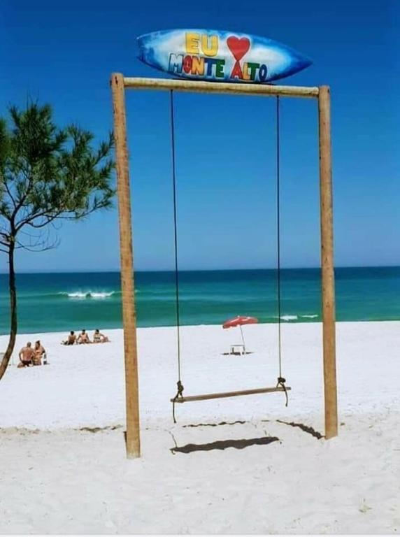 a swing on a beach with people on the beach at Casa Sol & Mar in Arraial do Cabo