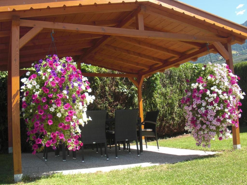 a wooden pergola with chairs and purple and white flowers at Garni Unterhaslerhof in Merano