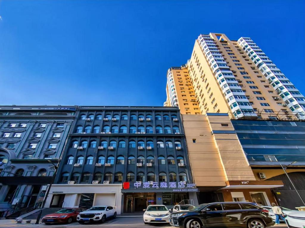 een groot gebouw met auto's ervoor geparkeerd bij Zhongmai Yunting Hotel in Harbin