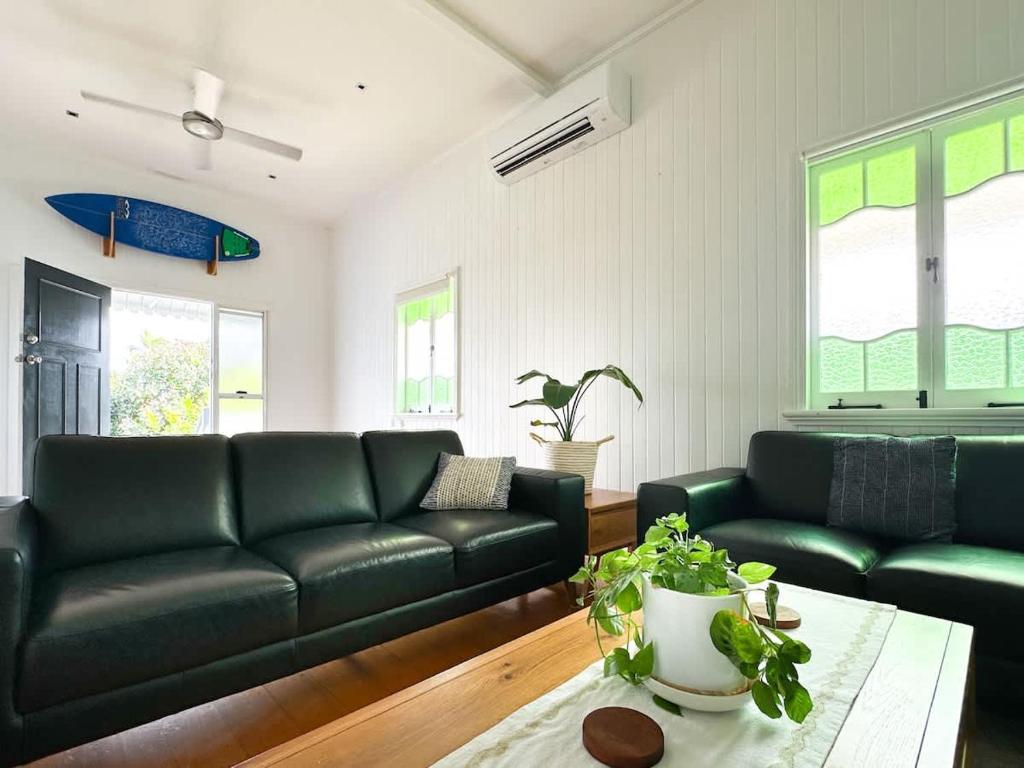 a living room with black leather couches and a table at Classic City Queenslander - Walk to Esplanade in Cairns North
