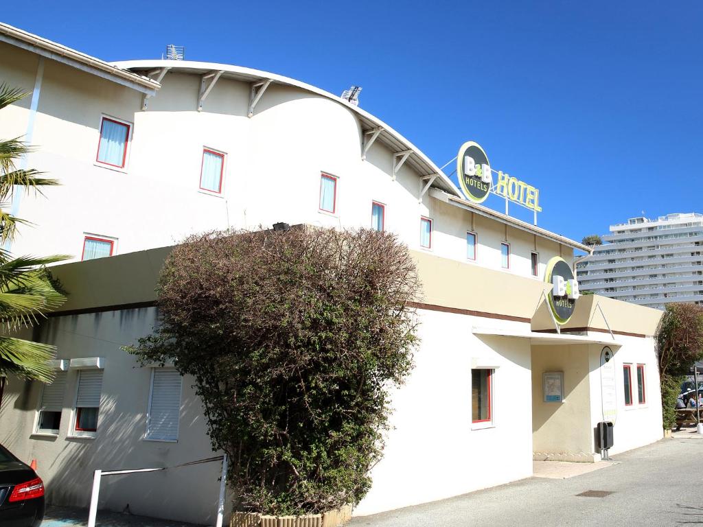 um edifício branco com um arbusto à frente em B&B HOTEL Villeneuve Loubet Plage em Villeneuve-Loubet