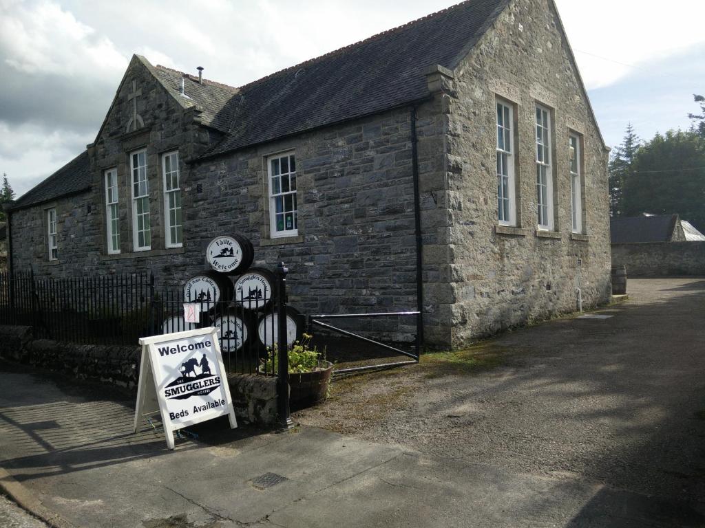 un antiguo edificio de piedra con un cartel delante en The Smugglers Hostel en Tomintoul