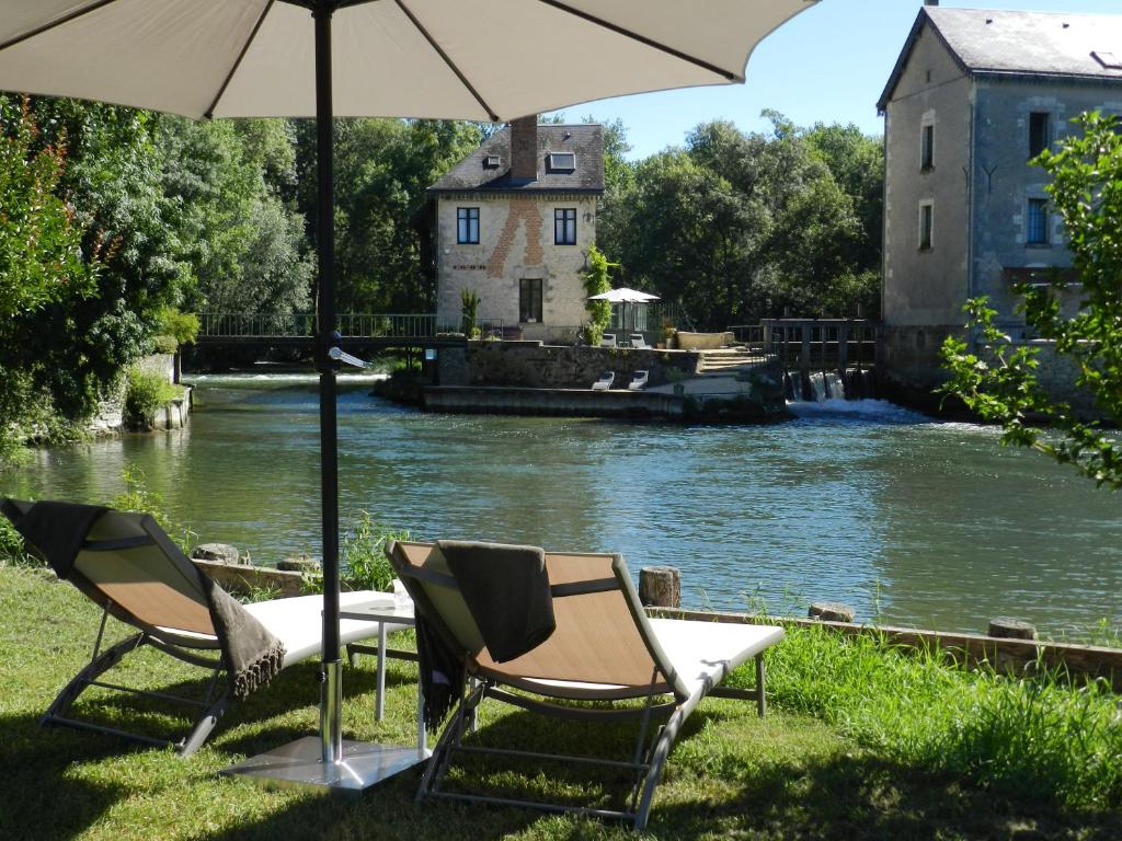two chairs and an umbrella next to a river at Moulin de la Chevriere in Saché