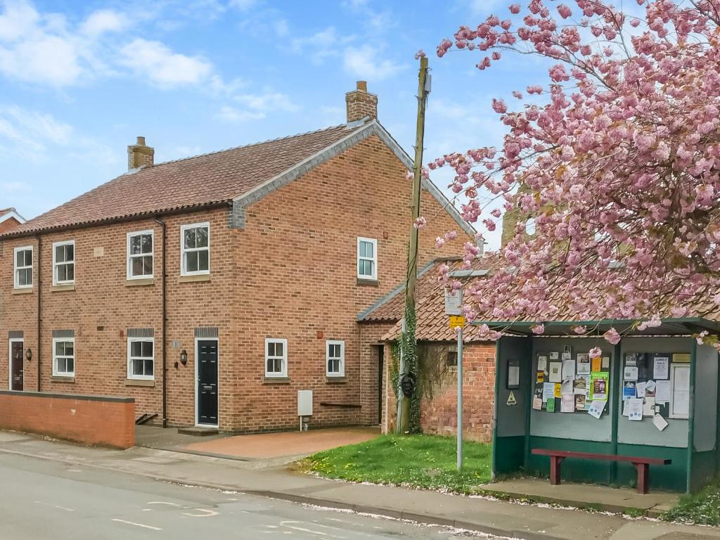 an old brick building with a kiosk in front of a tree at 1 Kirkby Cottages in Sheriff Hutton