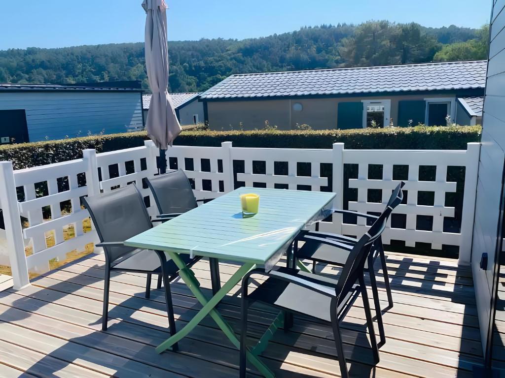 a table and chairs on a deck with a drink on it at Chalet Guerlédan in Caurel