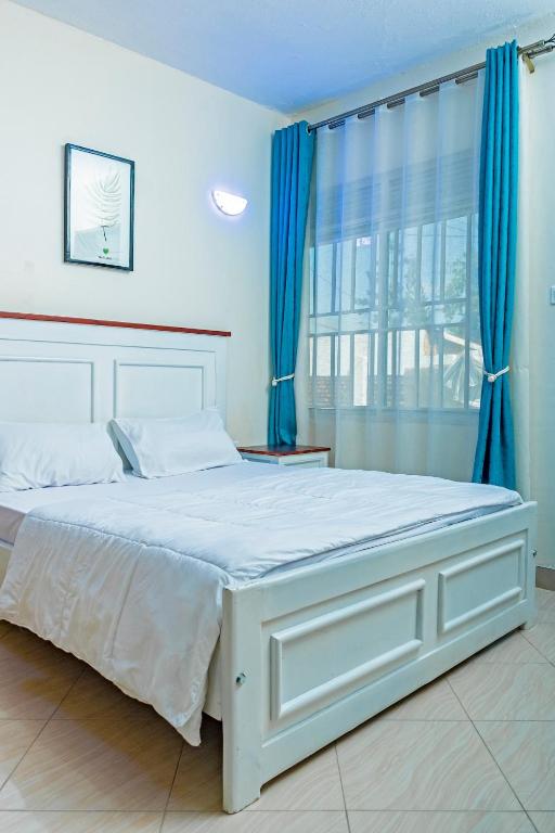 a bedroom with a large white bed with blue curtains at Bright & Airy 2BR Haven in Kampala