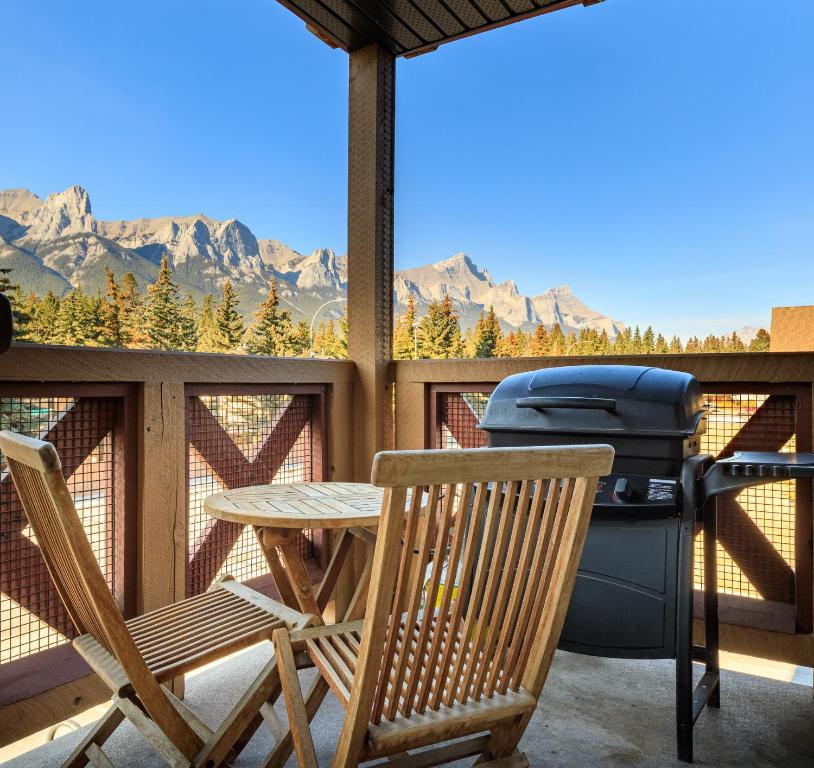 a patio with a grill and two chairs and a table at Bluebird - Spacious Luxury Shared Rooftop Hot Tub in Canmore