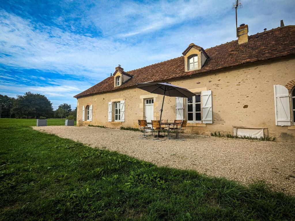 a house with a table and an umbrella in front of it at Maison de vacances en Brenne avec piscine partagée, grand jardin et tout confort inclus - FR-1-591-329 in Bélâbre