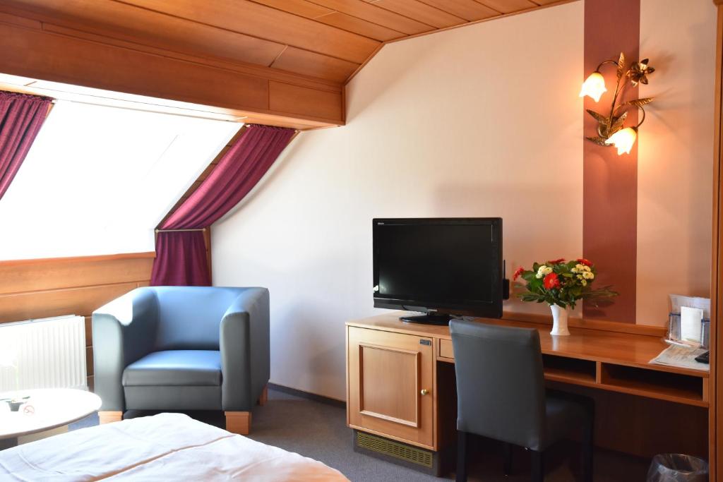 a hotel room with a bed and a tv and a chair at Hotel Haus Tiefenbach in Bullange