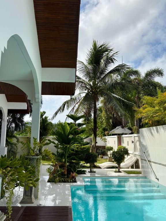 a swimming pool next to a building with palm trees at Villa Happy home in Rawai Beach