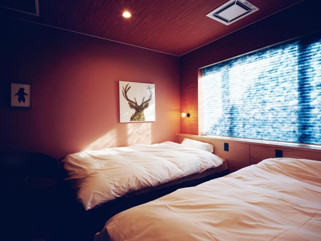a bedroom with two beds and a window with a tree picture at 地元酒屋が手がける一棟貸し宿 -霧ノ音- in Kushiro