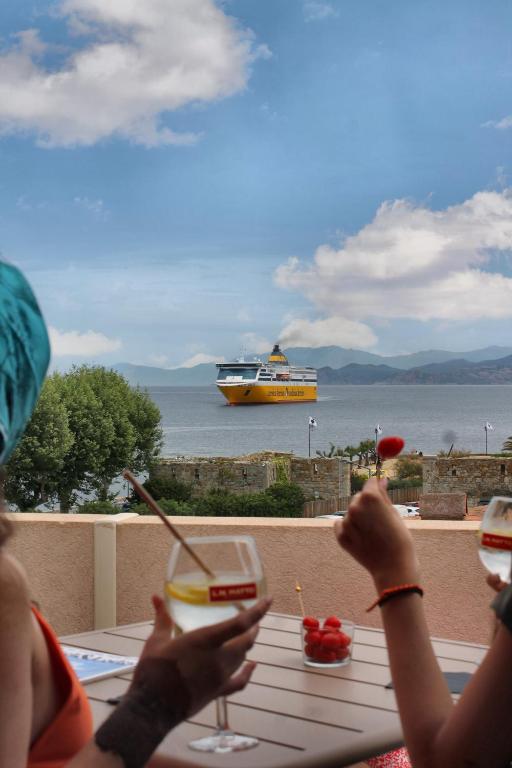 a group of people sitting at a table with a boat in the water at Hôtel & Spa Rocabella in LʼÎle-Rousse