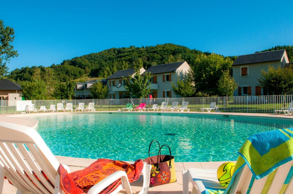 a swimming pool with two lawn chairs and a towel on them at Résidence Le Village Goélia in Saint-Geniez-dʼOlt