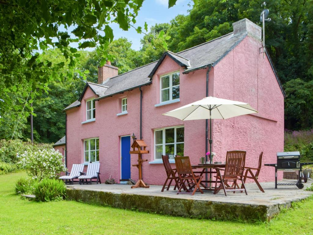 ein rosafarbenes Haus mit einem Tisch, Stühlen und einem Sonnenschirm in der Unterkunft Wood Cottage in Cheriton