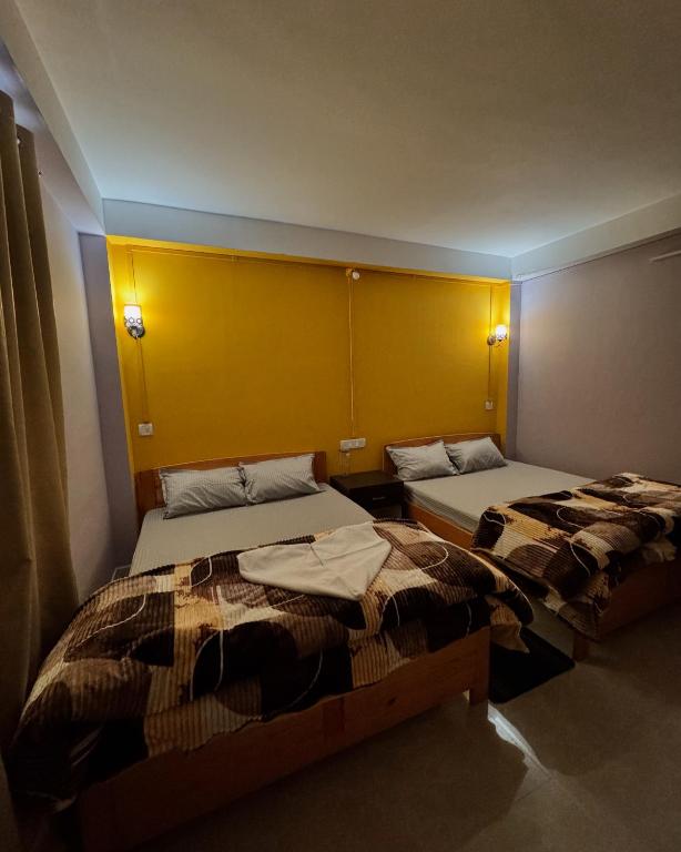 two beds in a room with a yellow wall at Tashi Khangsar in Tawang