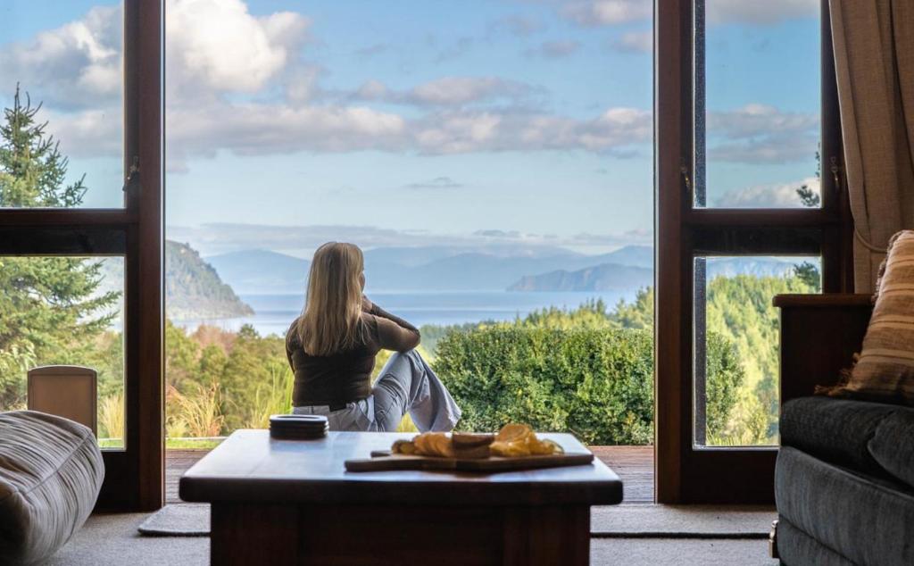 a woman sitting in front of a large window at Muirs Reef Lodge Kinloch holiday home Lake Taupo in Kinloch