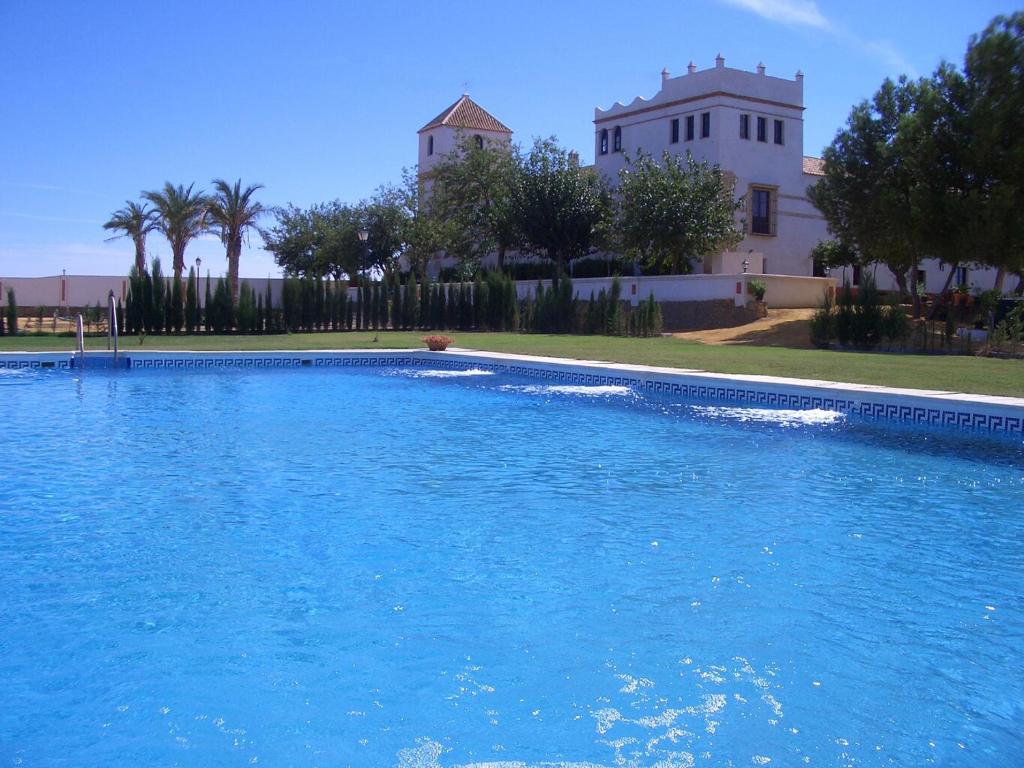 une grande piscine d'eau bleue devant un bâtiment dans l'établissement Hacienda Los Jinetes, à Carmona