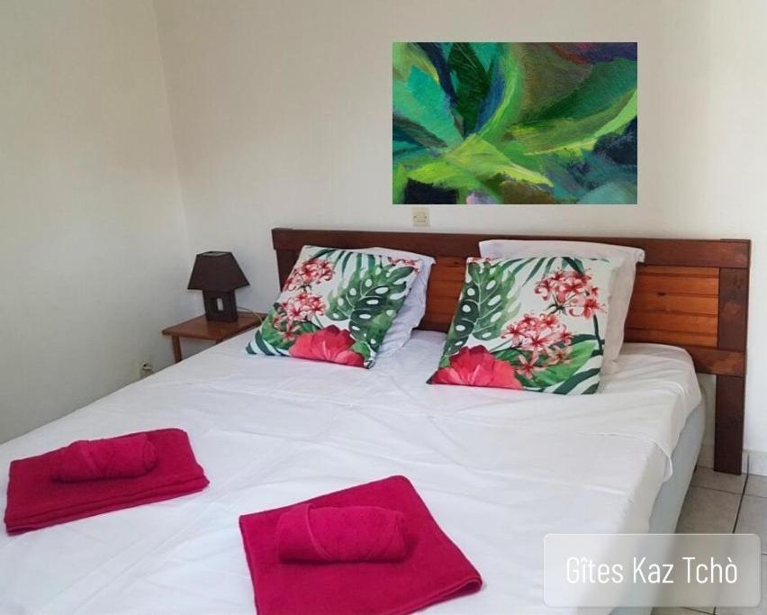 a white bed with two red pillows on it at Gîtes Kaz Tchò in Sainte-Anne