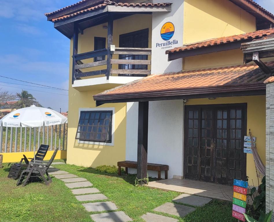 una casa amarilla y blanca con una silla y una sombrilla en PeruíBella Pousada, en Peruíbe