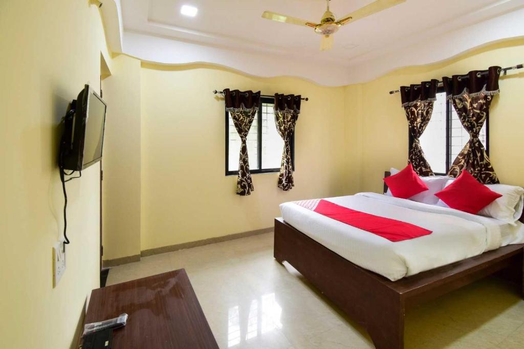 a bedroom with a bed with red pillows and a television at Hotel O Gokul Lodging in Pune