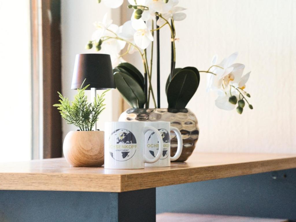 a table with two coffee mugs and a vase with plants at Ochsenkopf-apartment in Bischofsgrün