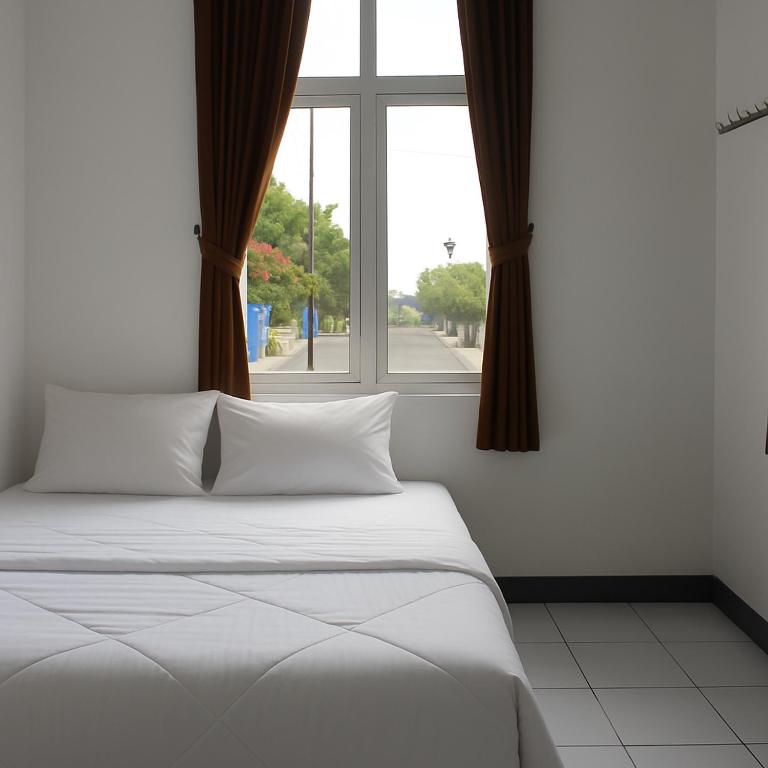 a bedroom with a white bed and a window at Hotel Griya Kopi in Pekalongan