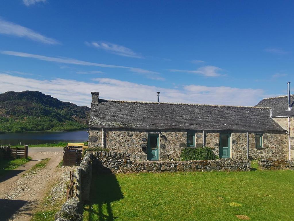 an old stone house with a lake in the background at The Grain Store in Aberarder
